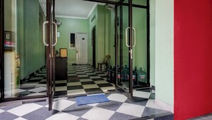 A hotel lobby with a checkered floor, glass doors, and a blue mat at the entrance. - Hotel O near Universitas Medan Area (Medan)