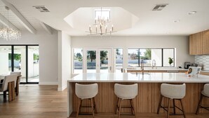 Een moderne keuken met een groot eiland, houten details en grote ramen met uitzicht op de omgeving.