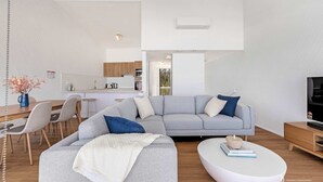 A modern living room with a grey sectional sofa, a white coffee table, and a dining area with a wooden table and chairs. - Direct Beachfront Townhouse (Malua Bay)