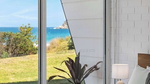 A bedroom with a large window overlooking a grassy area and the ocean. - Direct Beachfront Townhouse (Malua Bay)