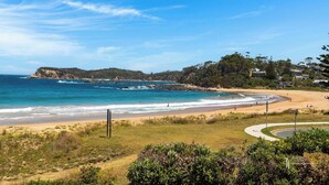 A coastal landscape with a sandy beach, a rocky outcrop, and a residential area with houses. - Direct Beachfront Townhouse (Malua Bay)