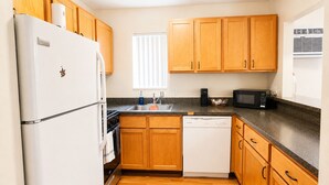 A compact kitchen with wooden cabinets, a white refrigerator, a dishwasher, a stove, and a microwave. - The Ann Arbor's Nest - Stylish Downtown Stay Near U-M, Dining & Attractions (Ann Arbor)