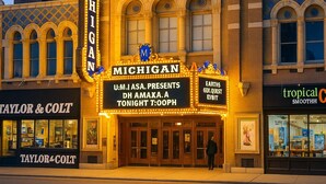 Ein Theater mit einer Litfaßsäule, die eine Vorstellung von U.M.I.A.S.A. und eine Präsentation von Dh Amaka bewirbt.