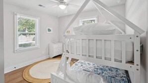 Una camera da letto bianca con un letto a castello, una ventola a soffitto, un comodino e una finestra con persiane.