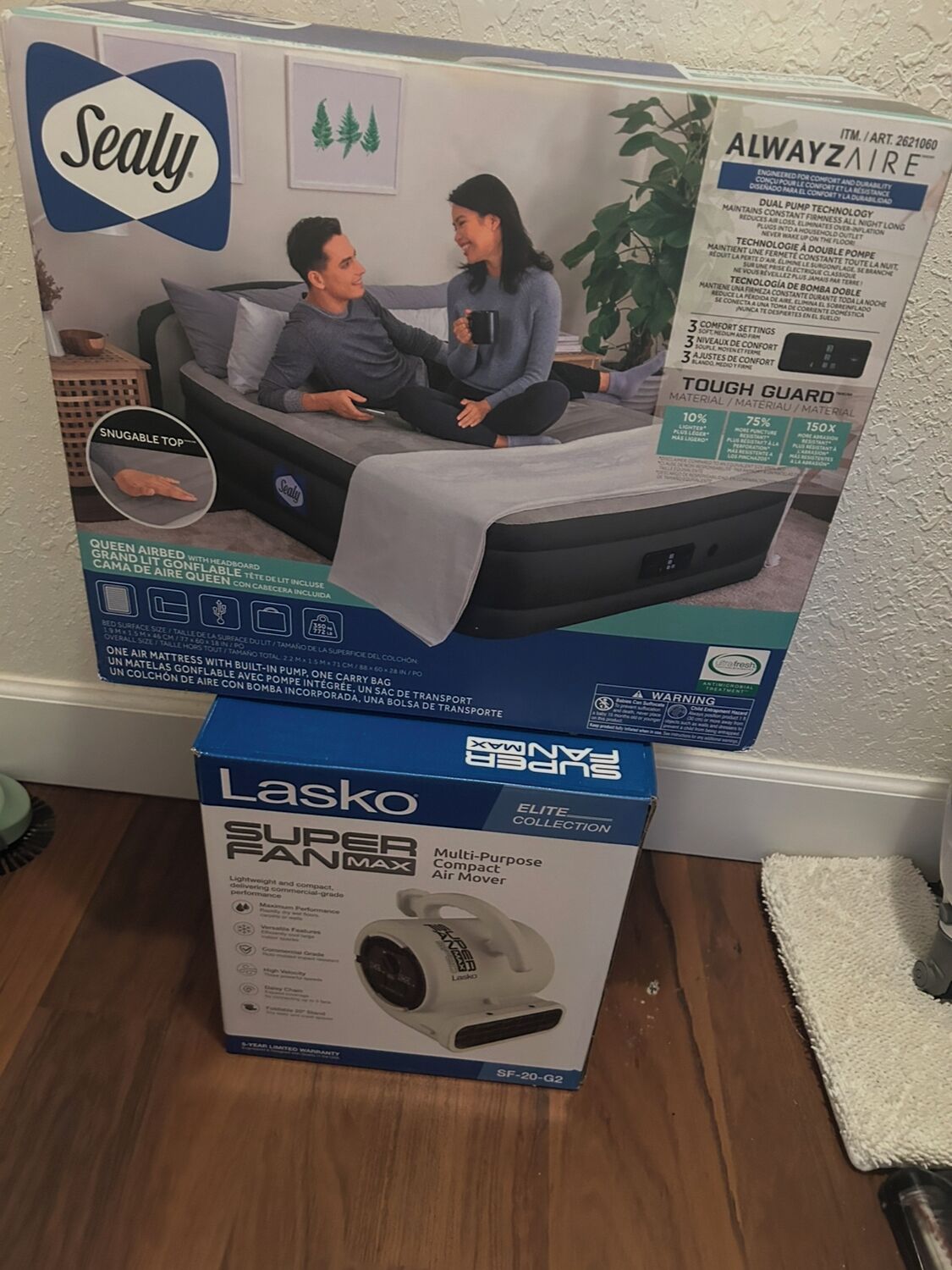 Un matelas Sealy dans sa boîte et un ventilateur Lasko.