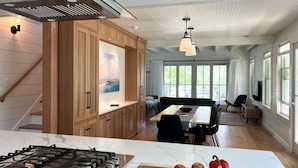 A modern kitchen with a gas stove, wooden cabinets, and a dining area with a table and chairs. - Away - Ocracoke Island (Ocracoke)