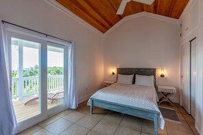 Een slaapkamer met een bed, een nachtkastje, een raam met uitzicht op een balkon, en een houten plafond.