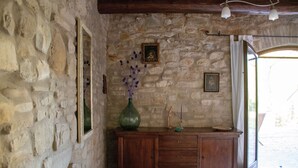 Un mur de pierre avec une armoire en bois, un tableau encadré et un vase rempli de fleurs violettes.
