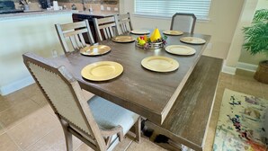 A dining area with a long wooden table set for six, surrounded by wooden chairs. A fruit bowl with grapes, a pear, and other fruits is on the table. - Cozy Family Retreat (Rosenberg)