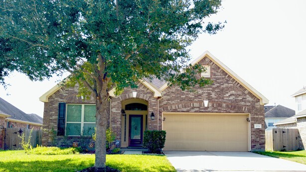 A two-story house with a brick facade, a front yard with a tree, and a garage. - Cozy Family Retreat (Rosenberg)