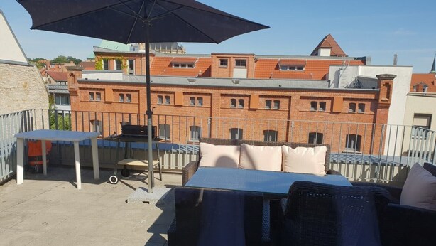 Terraza en la azotea con una mesa, sillas, una sombrilla y una parrilla.