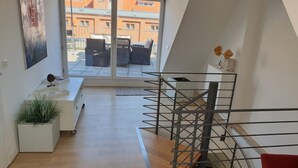 Un interior moderno con una escalera, un sofá blanco, una planta en maceta y vistas al exterior.