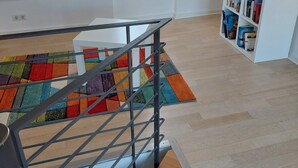 Un interior moderno con piso de madera, un tapete colorido, una escalera de metal y una estantería llena de libros.