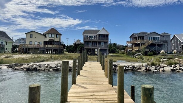 A wooden pier leading to a beachfront property with multiple buildings, including a large house with a balcony and a smaller structure with a porch. - Sundance - Ocracoke Island (Ocracoke)
