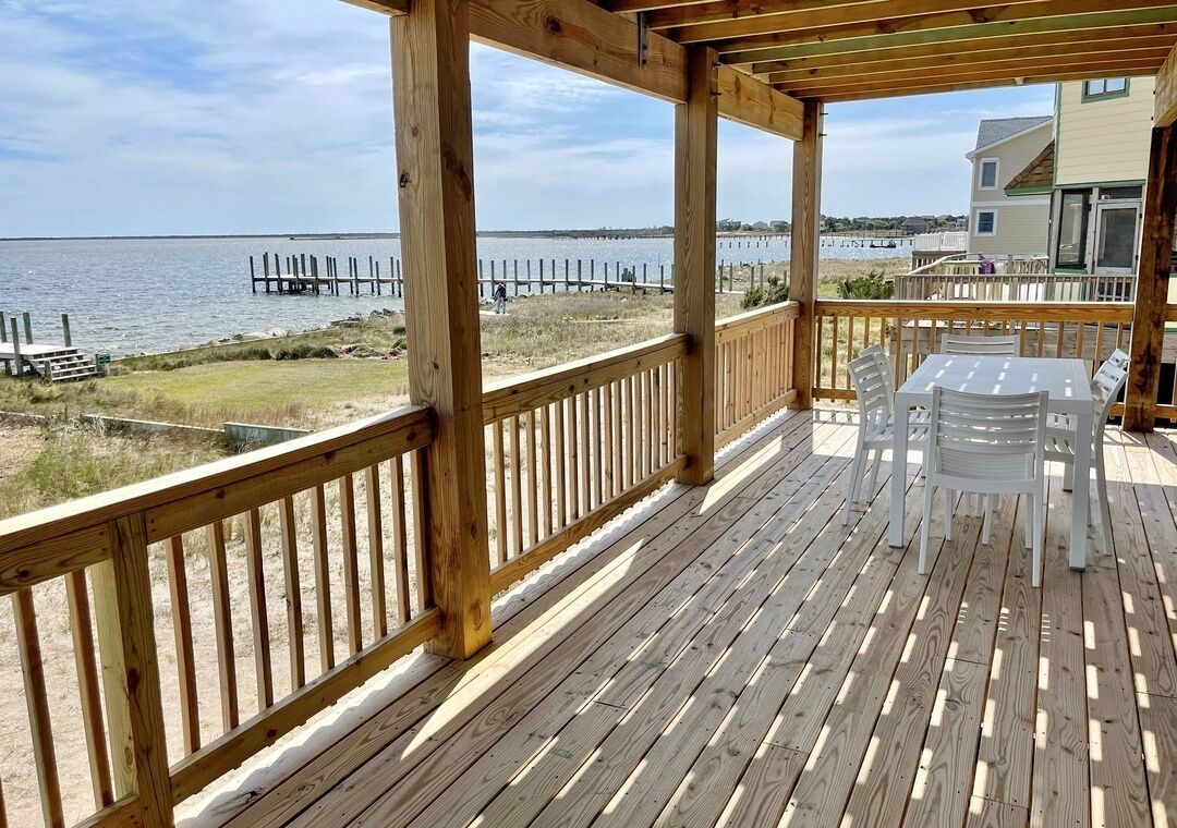 Una terraza de madera con mesa y sillas, con vistas a una playa y al agua.