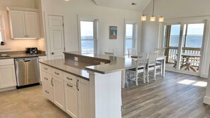 A spacious kitchen with a large island, white cabinetry, and a view of the ocean. - Sundance - Ocracoke Island (Ocracoke)