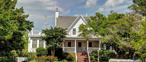 A two-story house with a front porch, a chimney, and a white picket fence.