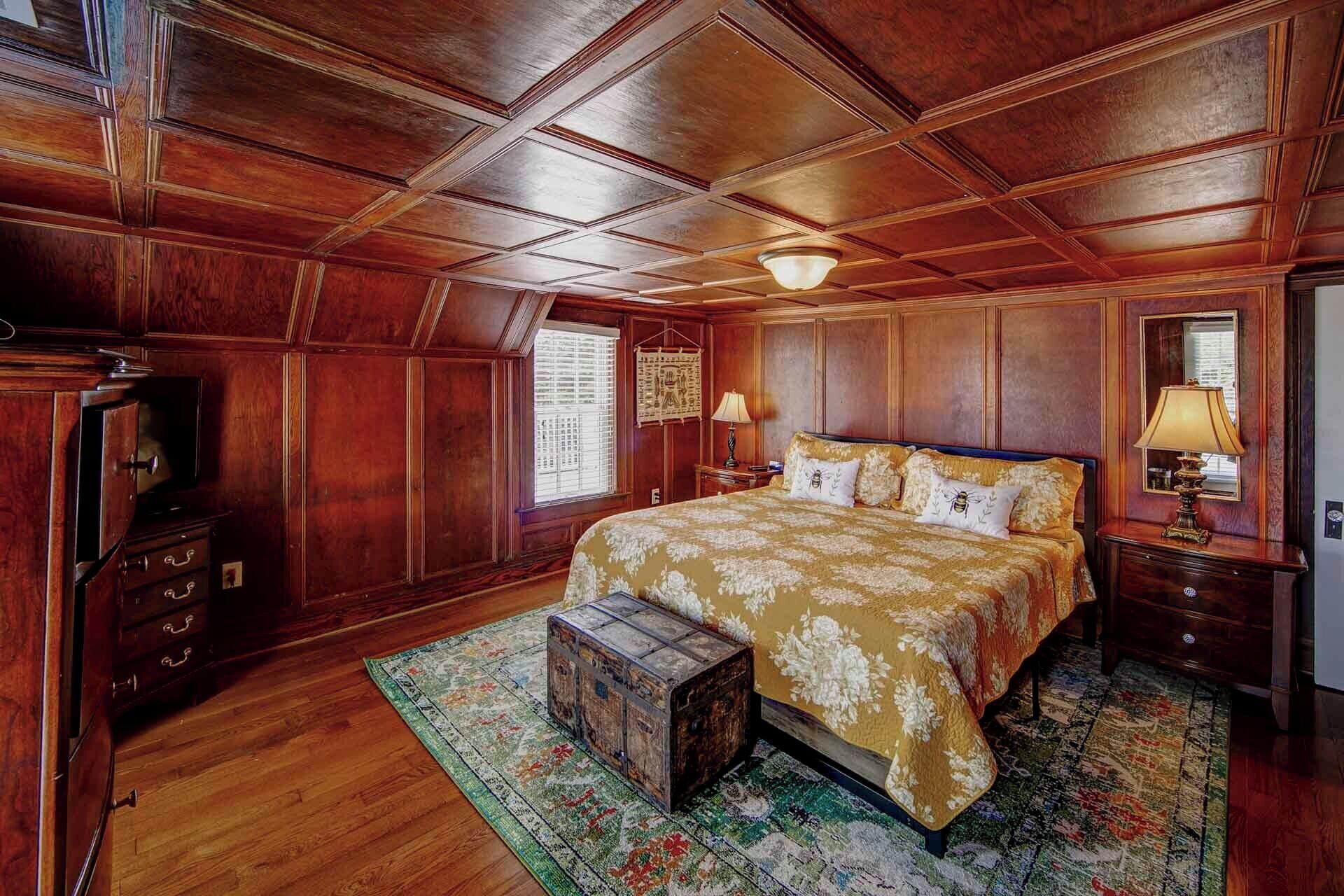 A bedroom with a large bed, wooden ceiling, and a vintage chest of drawers.