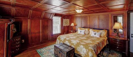 A bedroom with a large bed, wooden ceiling, and a vintage chest of drawers.