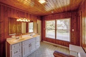 Ein Badezimmer in einer Holzhütte mit einem Doppelwaschtisch, einem großen Spiegel und einem Fenster mit Jalousien.