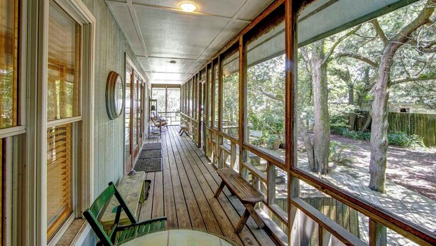 A covered porch with wooden benches and tables, large windows, and a view of trees. - Casa de Amor - Ocracoke Island (Ocracoke)