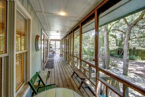 Une véranda avec des bancs et des tables en bois, de grandes fenêtres et une vue sur les arbres.