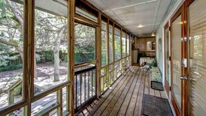 A covered porch with wooden railings and large windows, leading to a dining area with tables and chairs. - Casa de Amor - Ocracoke Island (Ocracoke)