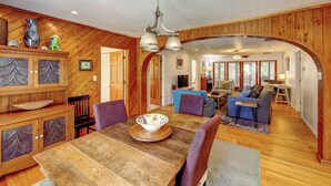 A spacious living area with wooden paneling, a dining table with chairs, a sofa, and a television. - Casa de Amor - Ocracoke Island (Ocracoke)
