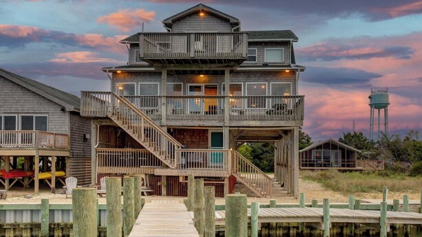 Una casa de madera de varios pisos con un balcón, una escalera y un muelle que lleva a un embarcadero.