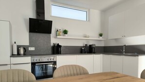 Eine moderne Küche mit weißen Schränken, einer schwarzen Dunstabzugshaube, einem eingebauten Backofen und einem Essbereich mit Holztisch und Stühlen.
