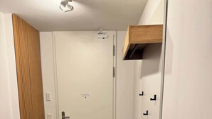Ein kleiner, gut beleuchteter Raum mit Holzboden, einer weißen Tür und einer Bank an der Wand.