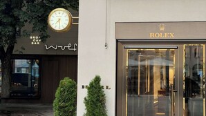 Ein Rolex-Geschäft mit einer Uhr und zwei Kübelpflanzen vor der Fassade.