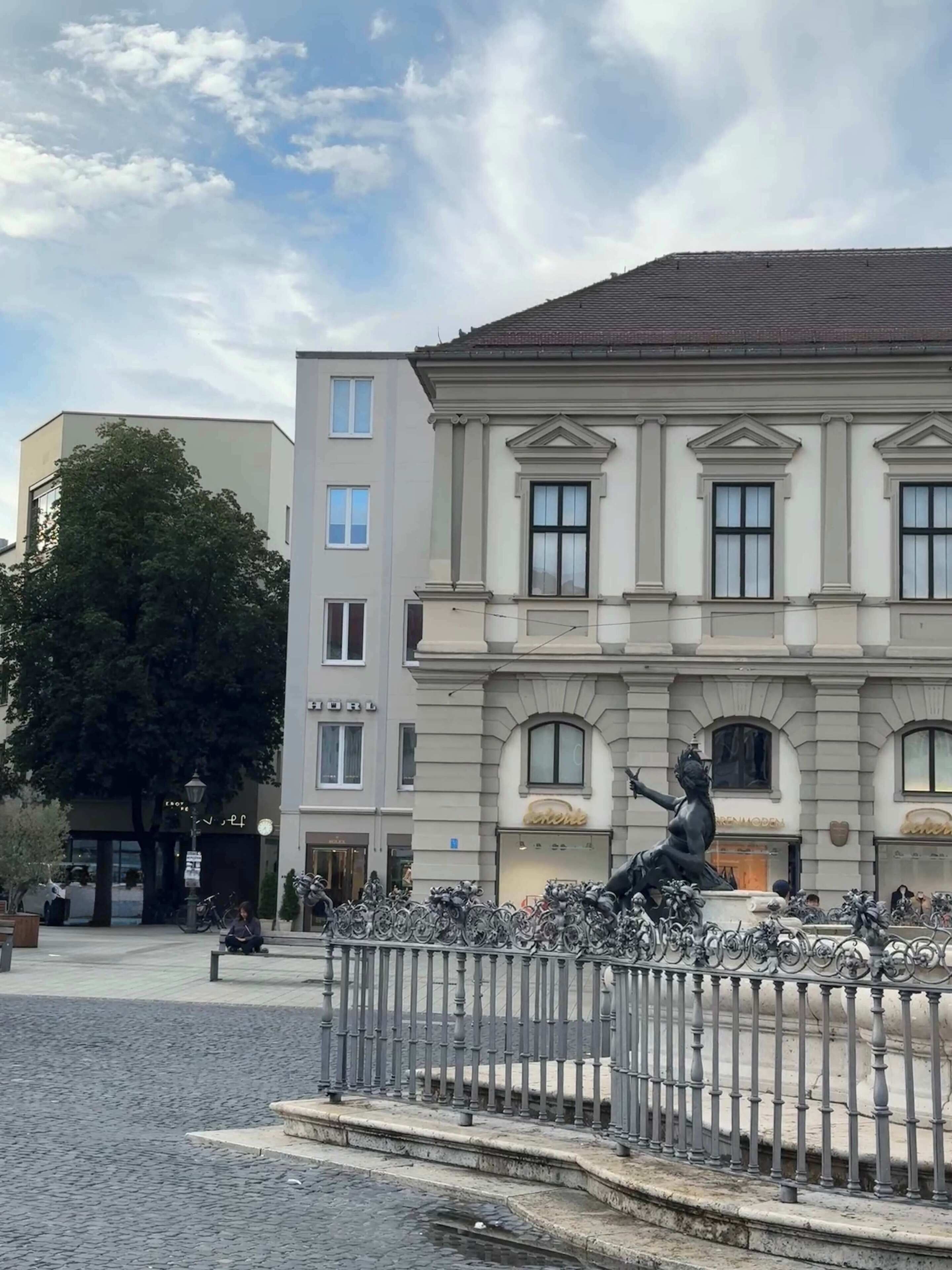 A building with classical architecture, a statue in front, and a cobblestone street.