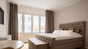 A bedroom with a large bed, a bedside table, a chair, and a window with curtains. - Luxury Suite "Augusta Vindelicum" | Rathausplatz Augsburg | A/C | Elevator (Augsburg)