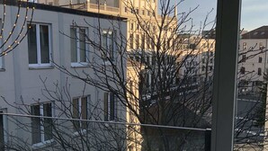 Vista de un edificio con una torre de reloj y una cúpula, visible a través de una ventana con ramas desnudas de árboles en primer plano.