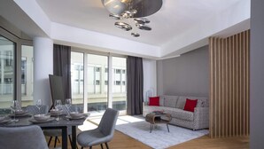 Una sala de estar moderna con comedor, ventanas amplias y un sofá con cojines rojos.