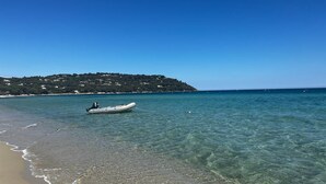 Uma praia com águas cristalinas, um barco e uma colina distante com edifícios.