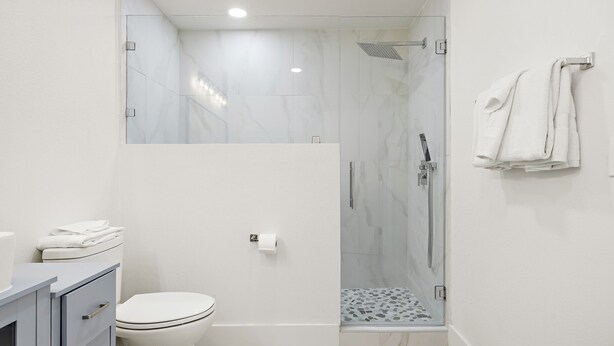 Een moderne badkamer met een douche met glazen wand, een toilet en een wastafel met lades.