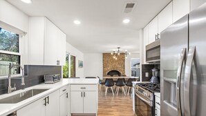 A modern kitchen with white cabinets, a stone fireplace, and a stainless steel refrigerator. - Spacious 4BR South Austin Home Minutes to Downtown (Austin)