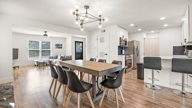 A modern kitchen with a central island, a dining area with a wooden table and black chairs, and a bar area with stools. - Spacious 4BR South Austin Home Minutes to Downtown (Austin)