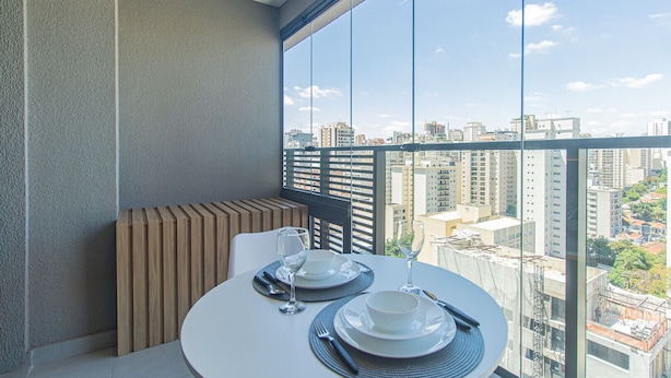 A balcony with a table set for two, a chair, and a view of a cityscape through large windows. - Near Allianz Parque Sp-p1803b (São Paulo)