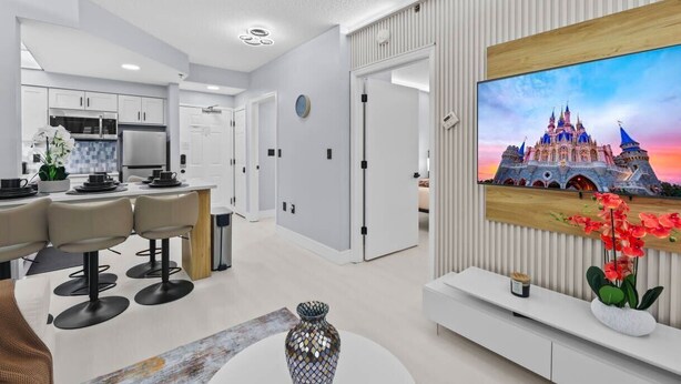 Een moderne woonkamer met een eethoek, een aan de muur bevestigde televisie en een keuken op de achtergrond.