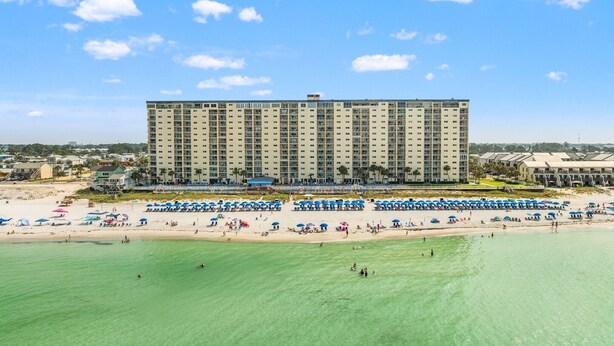 A large hotel with multiple floors, a beach with numerous umbrellas, and a clear view of the ocean. - AWESOME OCTOBER DEAL- ANY WEEK=1400 Total! 5star/Beachfront/FREE Beach Chairs! (Panama City Beach)