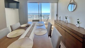 Una zona de menjador moderna amb una taula gran, caires i vista al mar a través de grans finestres.
