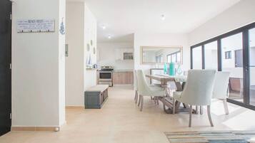 Een moderne keuken met witte kasten, een eethoek met een tafel en stoelen, en een groot raam met uitzicht.