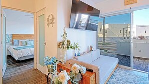Ein modernes Hotelzimmer mit Bett, Sofa, Fernseher und einem Balkon mit Blick auf den Strand.