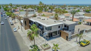 Un edificio commerciale dal design moderno, con un evidente cartello 'UER', situato in una zona costiera urbana con palme e vista sull'oceano.