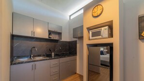 Una cucina moderna con mobili grigi, un piano di lavoro nero, un forno a microonde e una sveglia appesa al muro.