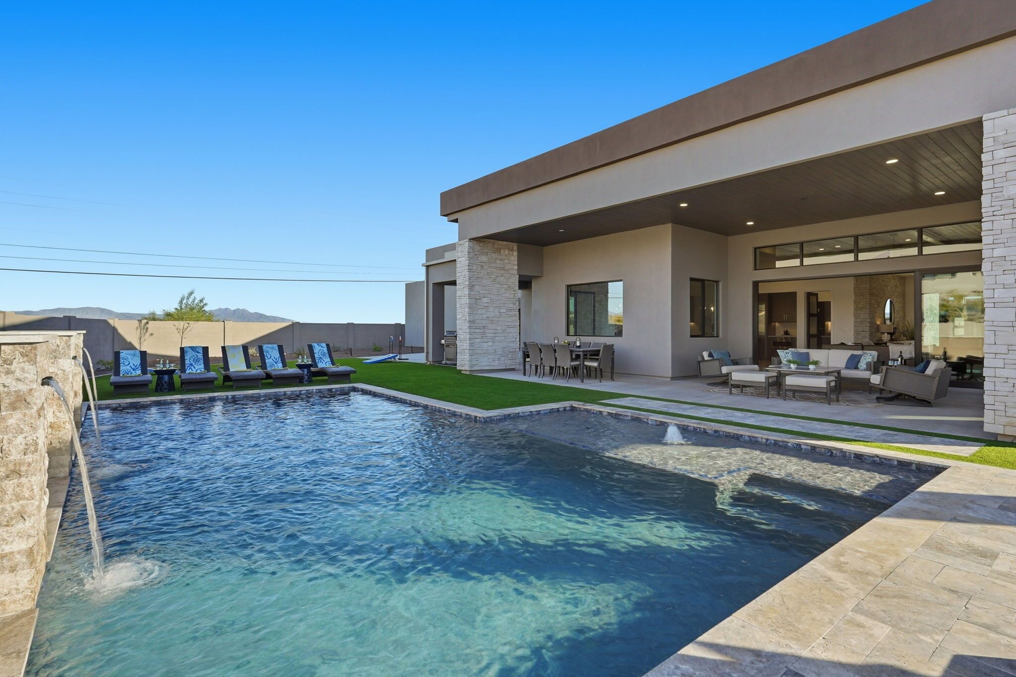 A modern house with a swimming pool, outdoor seating, and a stone facade.