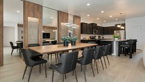 Une cuisine moderne avec des meubles de couleur sombre, un îlot central en bois et un coin repas comprenant une longue table et des chaises noires.